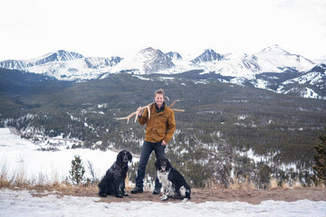 stephan and his dogs in front of snowy mountains with a large elk antler over his shoulder
